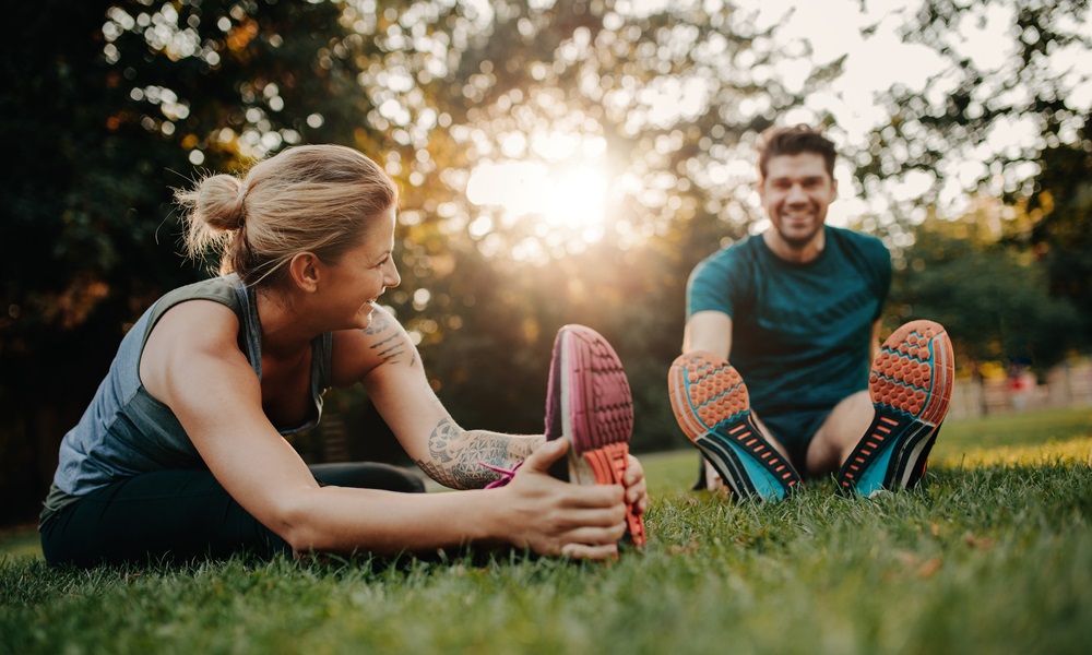 Fitness couple stretching outdoors in park. Young man and woman exercising together in morning.