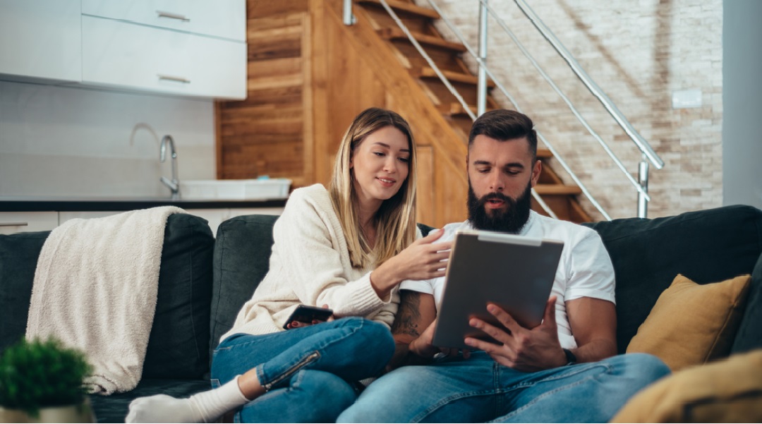 a man and woman sitting on a sofa looking down at an ipad together