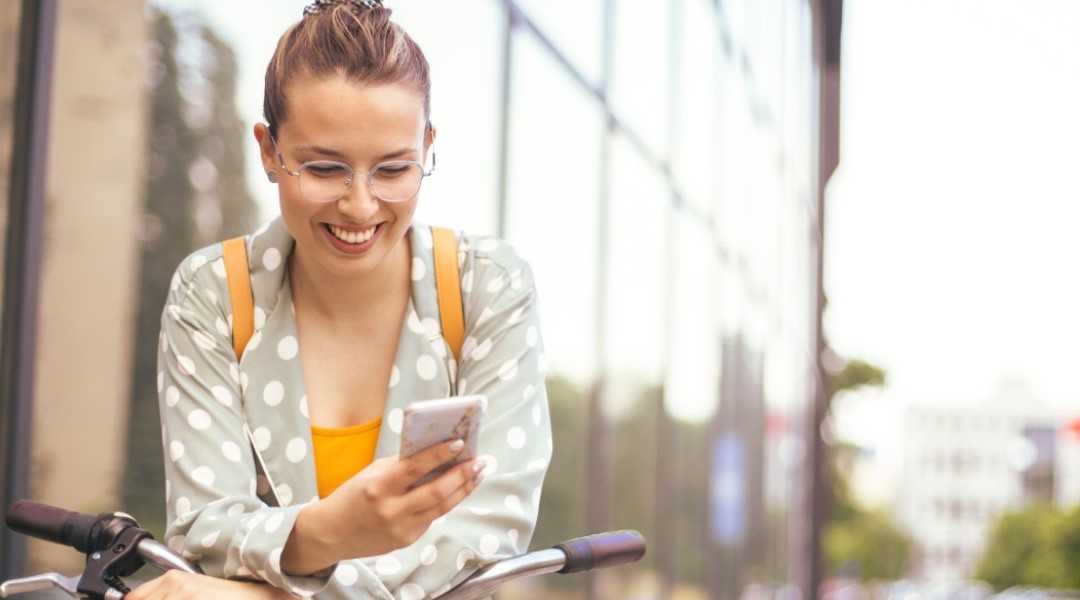 Lady with glasses leaning on her bike smiling at her phone